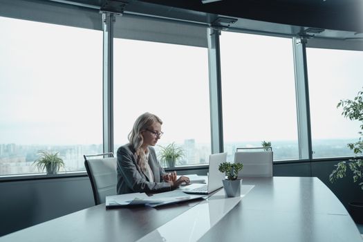 一位带着笔记本电脑的女人在明亮、现代化、有大窗户的办公室里工作