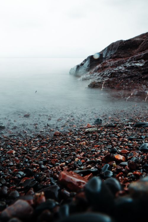 Free Serene rocky shoreline with mist over calm sea, capturing tranquility in nature's scene. Stock Photo