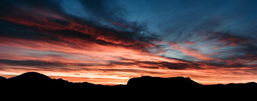 Panoramic view of horizon with mountain silhouette under vibrant sundown sky with clouds