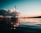 Rippling surface of calm water with small boat floating against cloudy sky at sundown