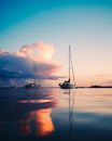 Tranquil smooth surface of sea reflecting sunset sky and yachts floating in twilight