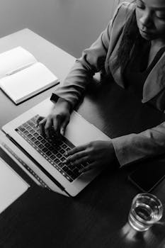 Woman working on a laptop in a grayscale office setting, capturing a professional and focused mood.