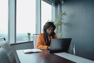 Woman in Orange Blazer Sitting at the Table Using Macbook