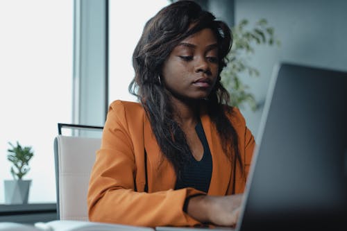 Woman in Orange Blazer Using a Laptop Computer