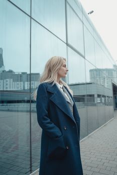 一位穿着蓝色外套的自信女人若有所思地站在一座反光玻璃建筑旁