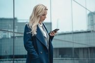一位穿着蓝色外套的职业女性在办公楼外使用智能手机