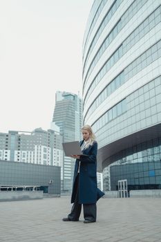现代办公楼外，一名女子穿着商务外套，正用笔记本电脑工作