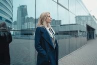 一位女商人穿着外套，自信地站在一座玻璃建筑前，背景是城市的摩天大楼