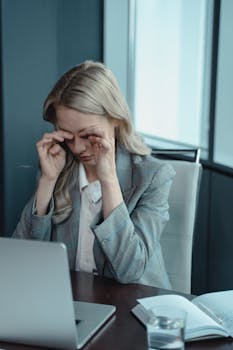 A businesswoman shows stress while working at her laptop in a modern office.