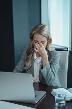 女商人坐在书桌前，面对一台笔记本电脑，显示出工作压力