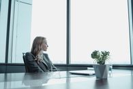 一位女商人穿着西装，望着现代化办公室的窗外
