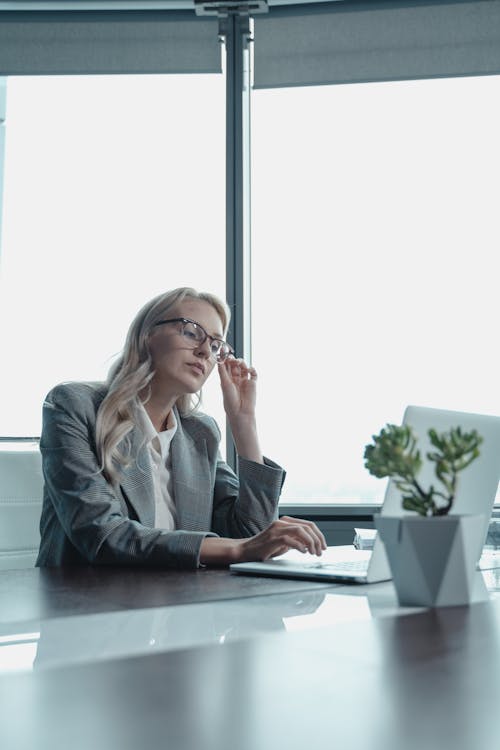 Free Woman Holding Her Eyeglasses While Sitting in Front of a Laptop  Stock Photo