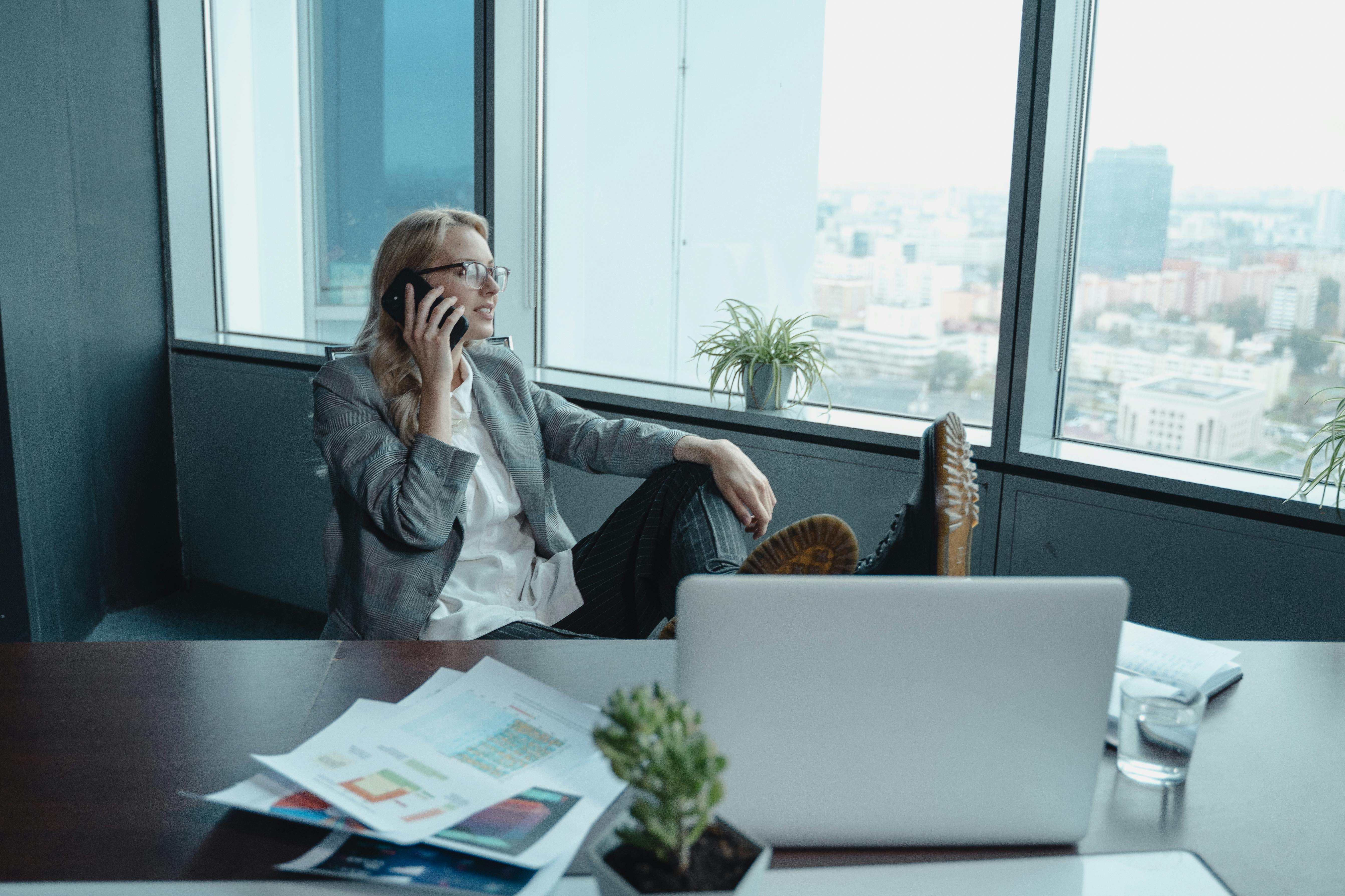 a woman in gray coat sitting on a swivel chair while having a phone call