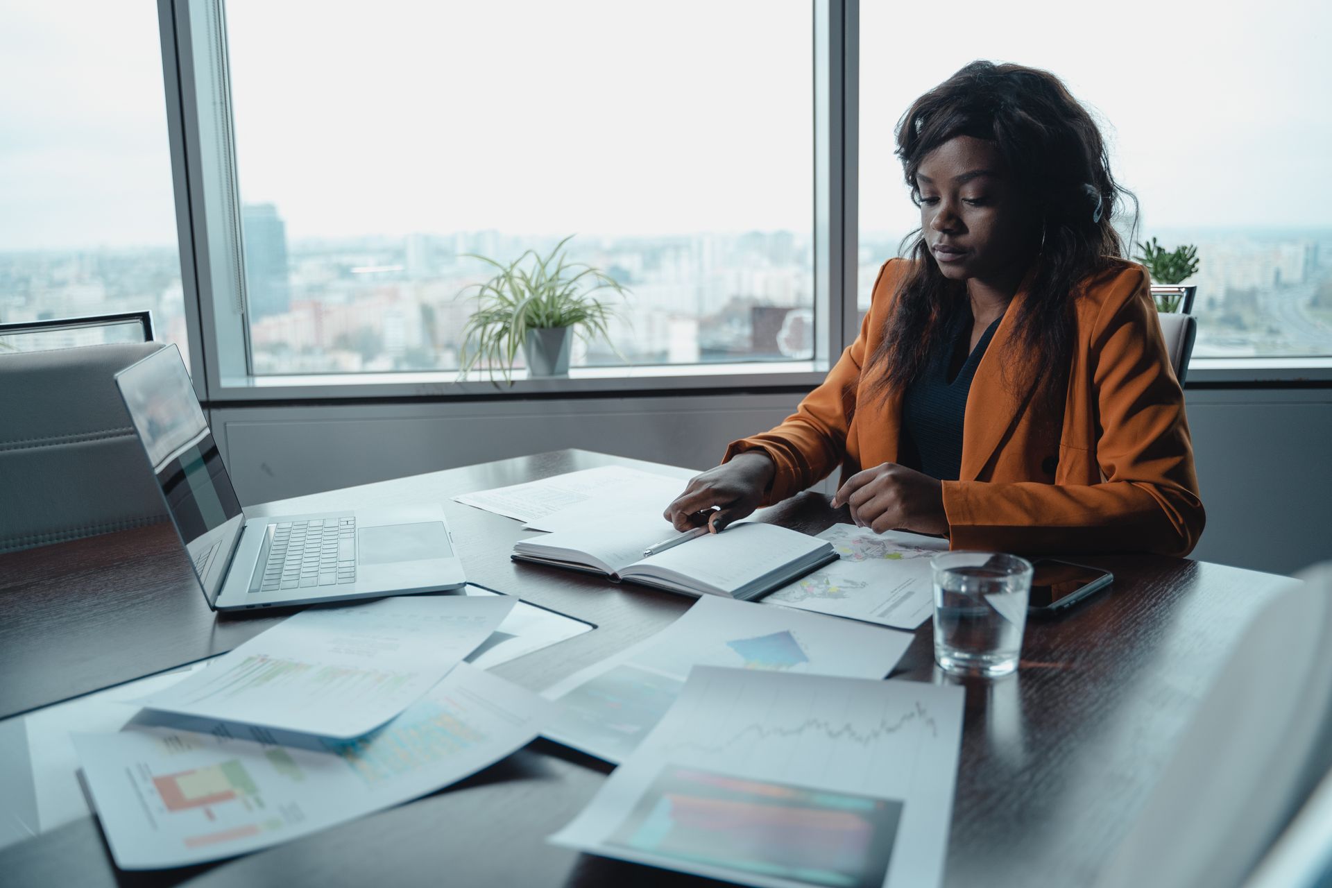 Focused businesswoman reviewing documents at a modern office desk with a city view.