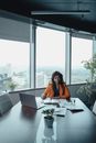女商人坐在高层办公室里，用笔记本电脑工作，窗外是城市景观