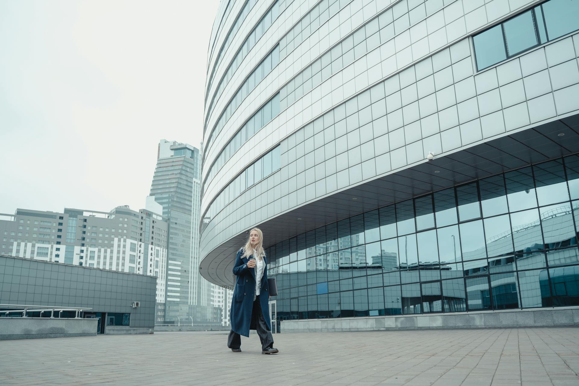 Businesswoman walking by glass-paneled modern urban office building with reflections.