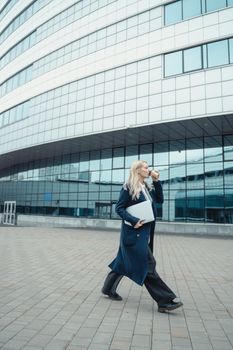 自信的女商人带着笔记本电脑和咖啡走出办公室，拥抱现代生活方式