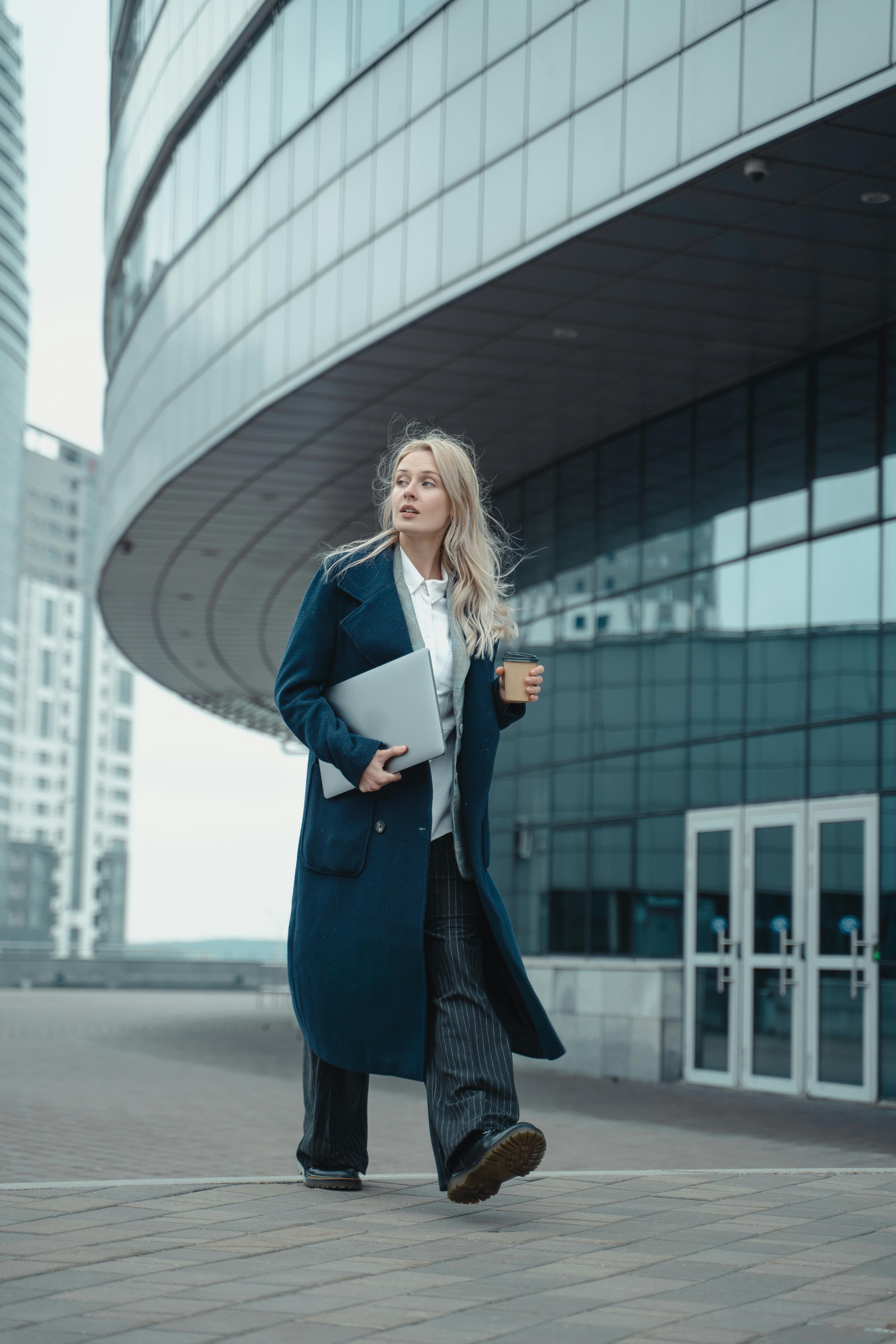 在城市环境中，一位现代女商人带着笔记本电脑和咖啡行走