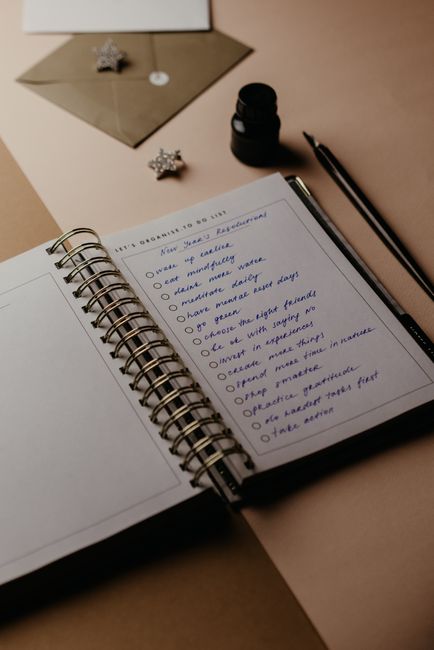 Spiral notebook open to New Year resolutions, with pen and accessories, in warm lighting.