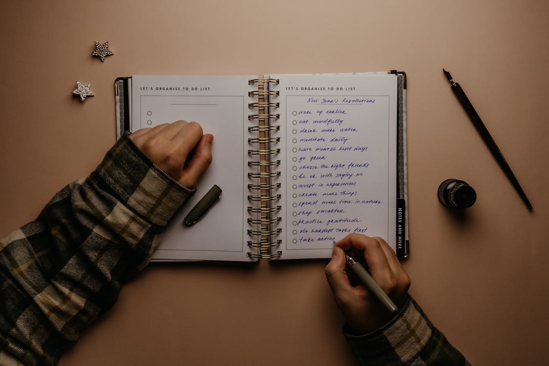 Person Holding Black Pen Writing on White Notebook