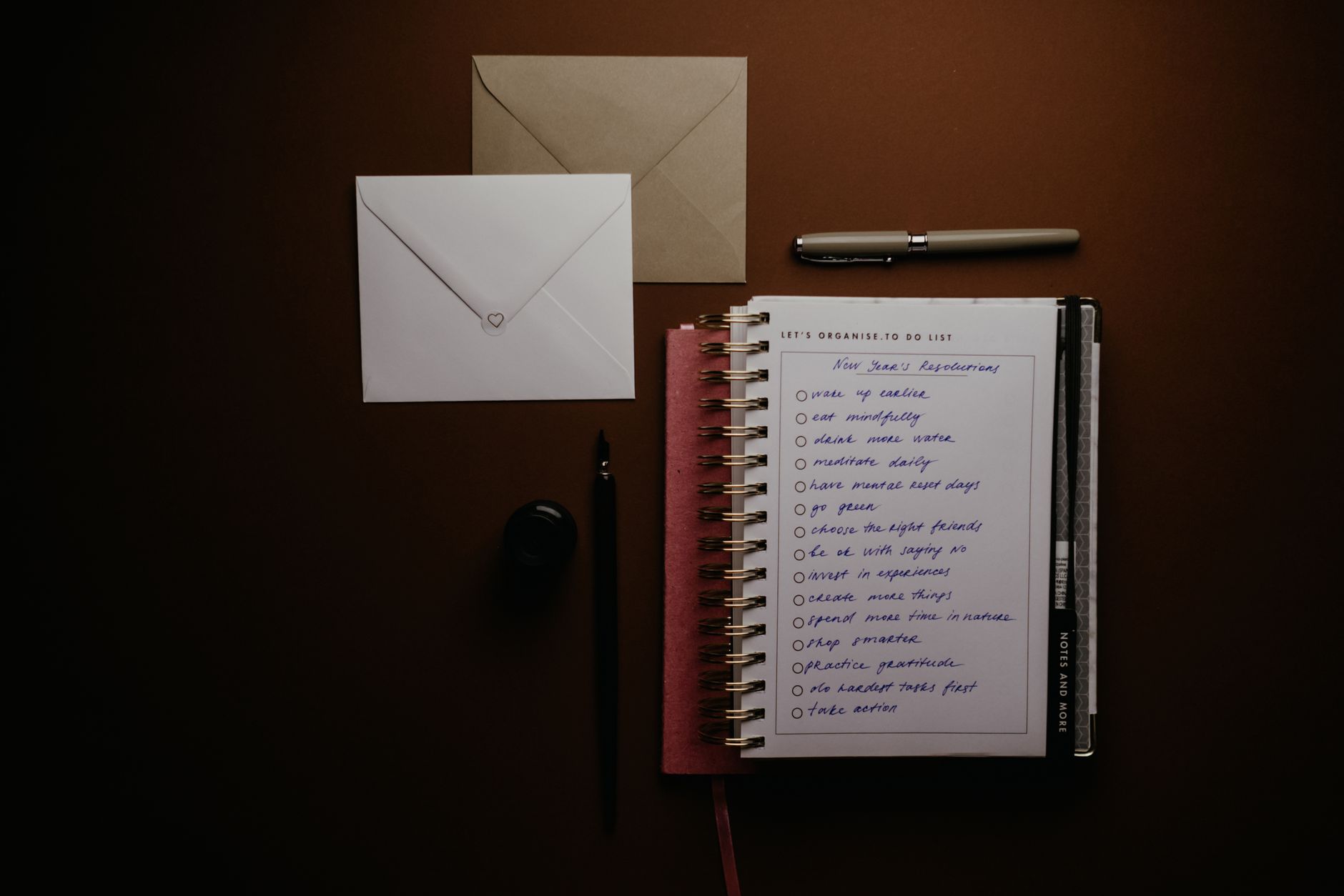 Overhead view of a to-do list notebook with New Year's resolutions, pens, and envelopes on a desk.