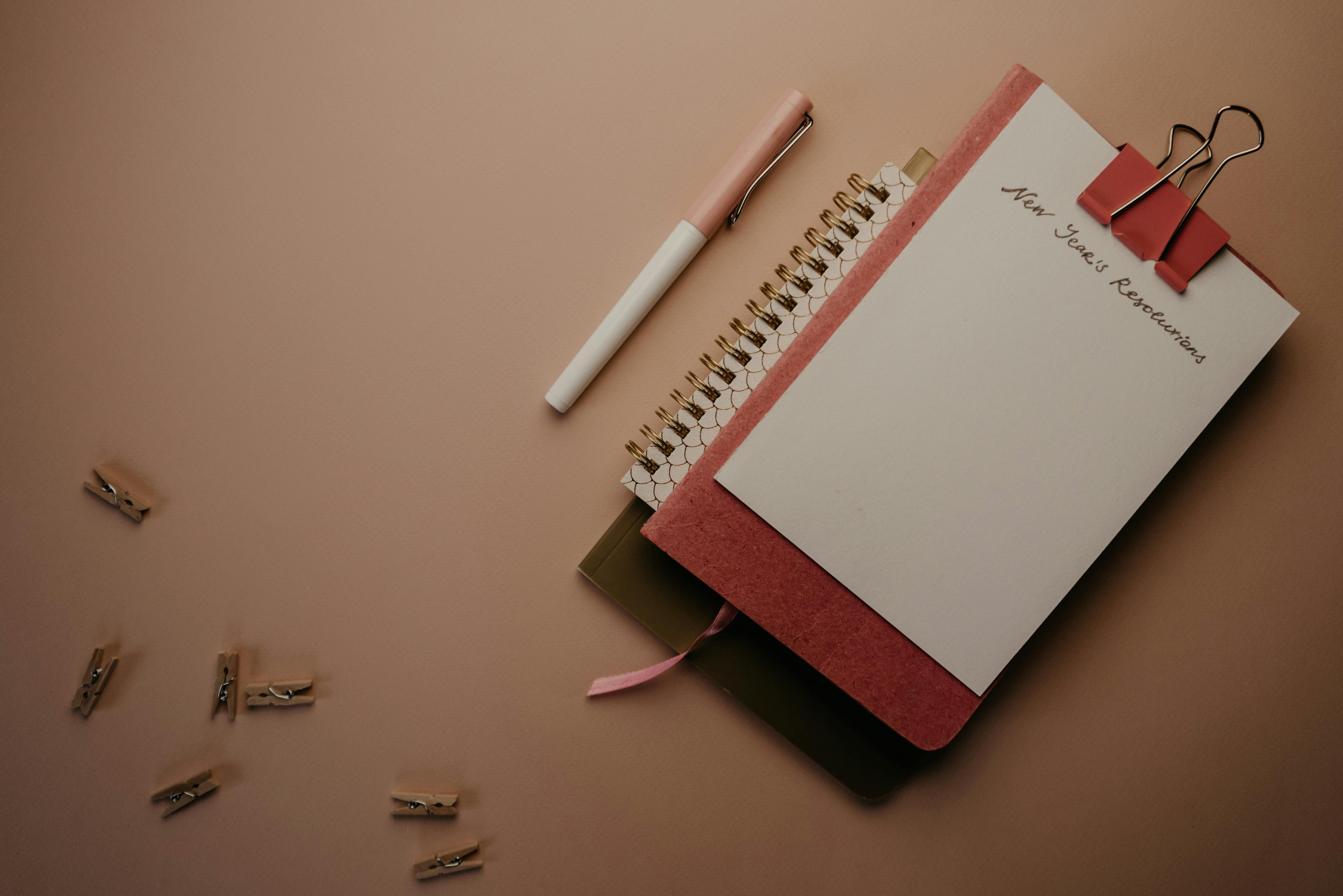 white and pink click pen beside white notebook