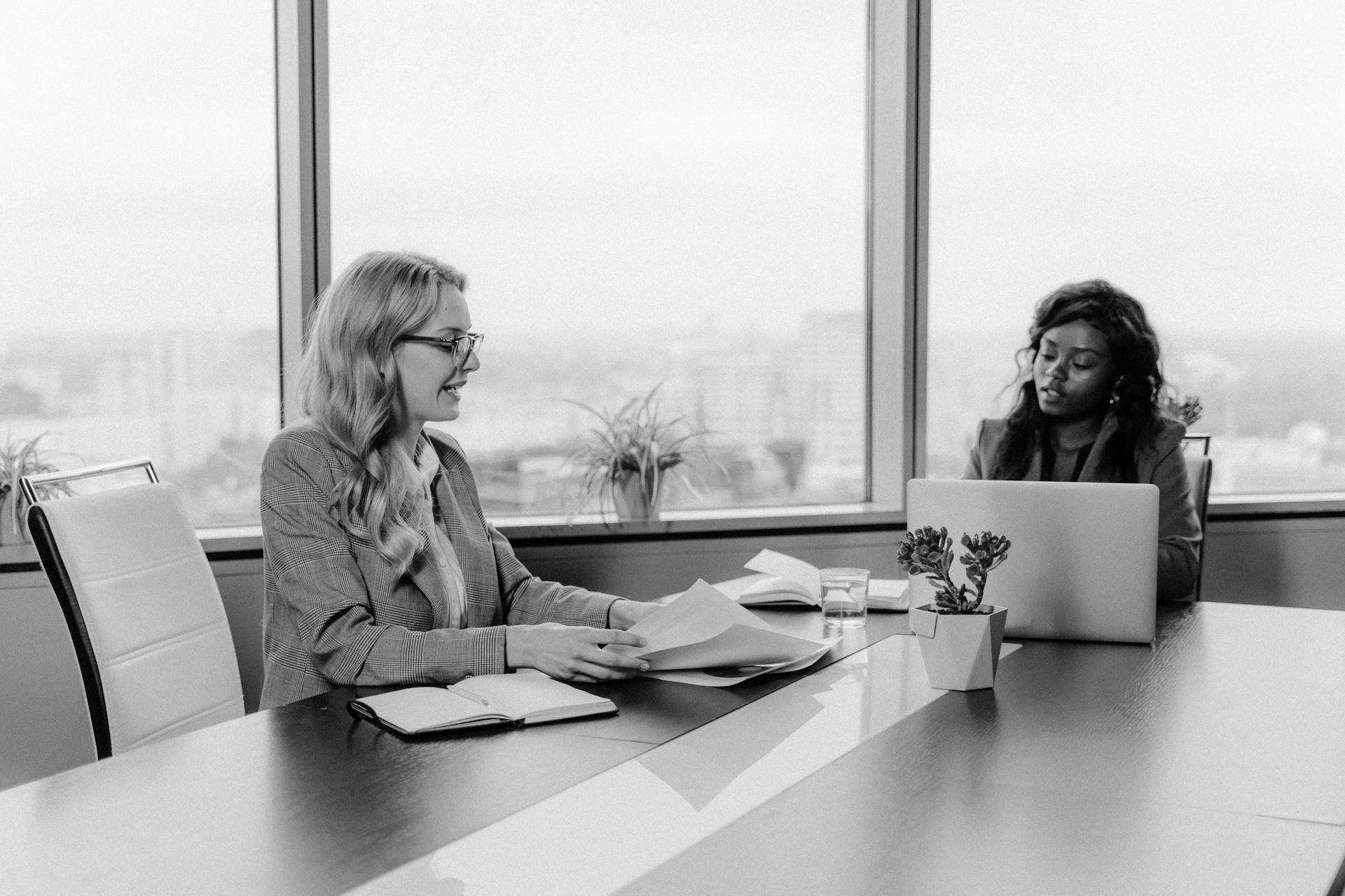 Two businesswomen in a corporate meeting discussing strategies in a modern office space.