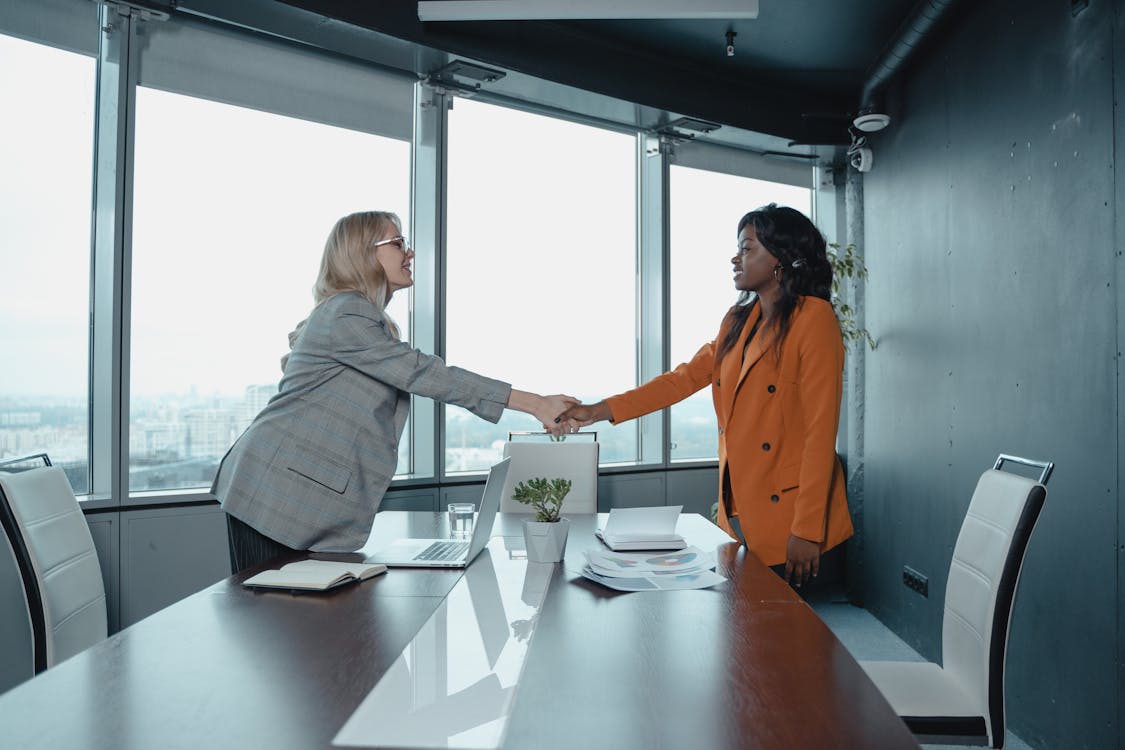 Woman in Orange Dress Shirt Standing Beside Woman in Gray Long Sleeve Shirt