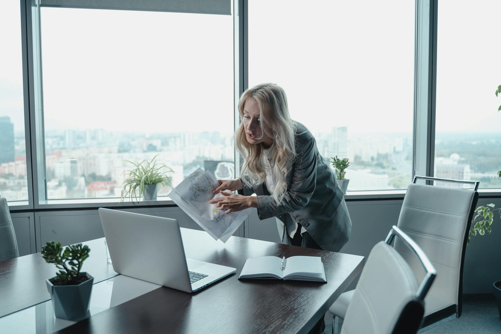 Professional businesswoman in modern office conducting virtual meeting with documents and laptop.