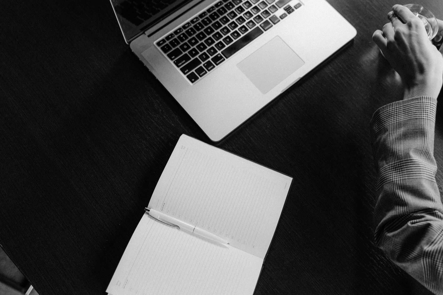 Professional workplace setting featuring a laptop, open notebook, and hand in grayscale.