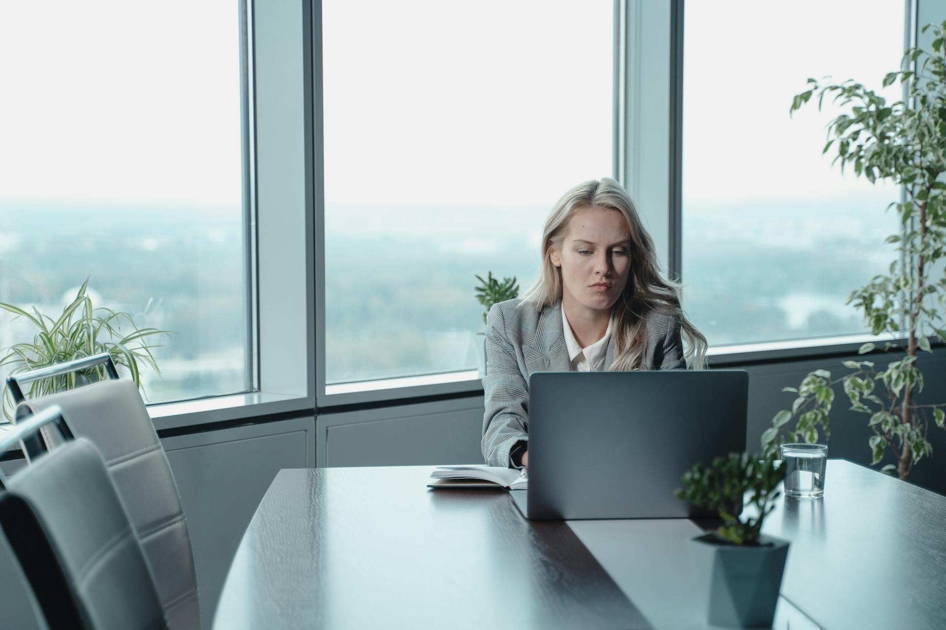 Professional woman working at a laptop in a modern office with large windows.