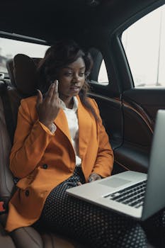 Businesswoman working on a laptop in the car, showcasing modern work flexibility and professional attire.