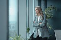 一位穿着优雅的职业女商人若有所思地从办公室的大窗户向外望去
