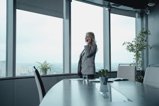 A professional woman makes a phone call in a sleek, modern office with city views.