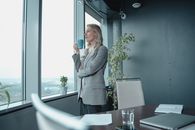 一位女商人端着咖啡，从现代化办公室的窗户俯瞰城市景观