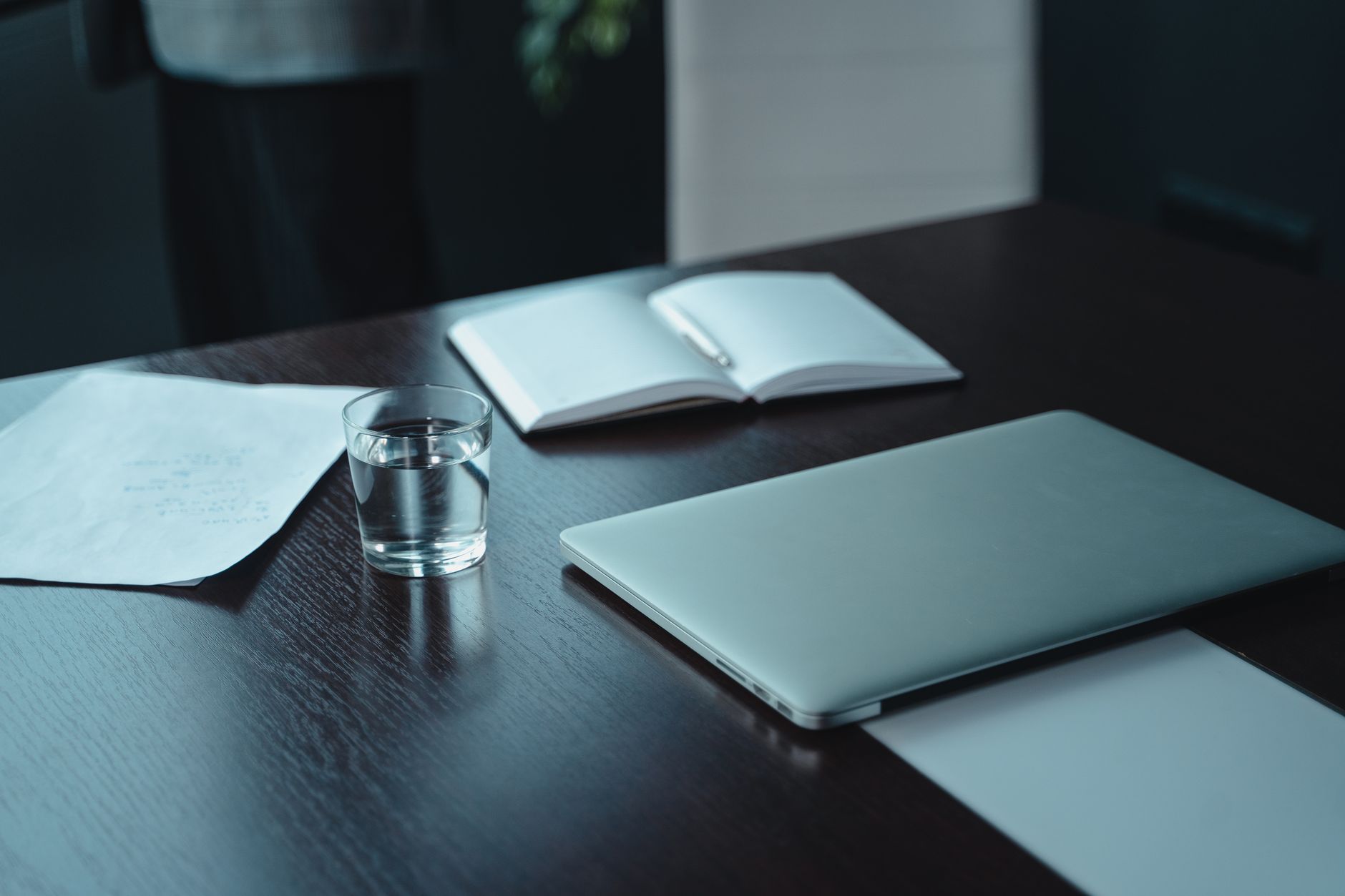 A modern workspace featuring a laptop, notebooks, and a glass of water on a wooden table.