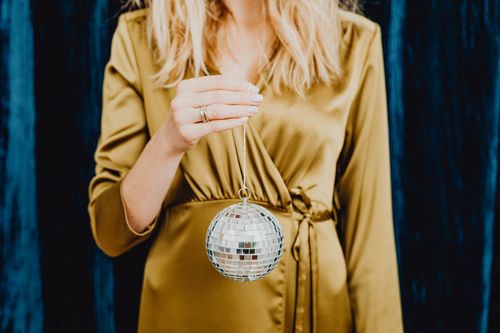 Free Stylish woman in gold dress holding a shimmering disco ball, perfect for festive occasions. Stock Photo