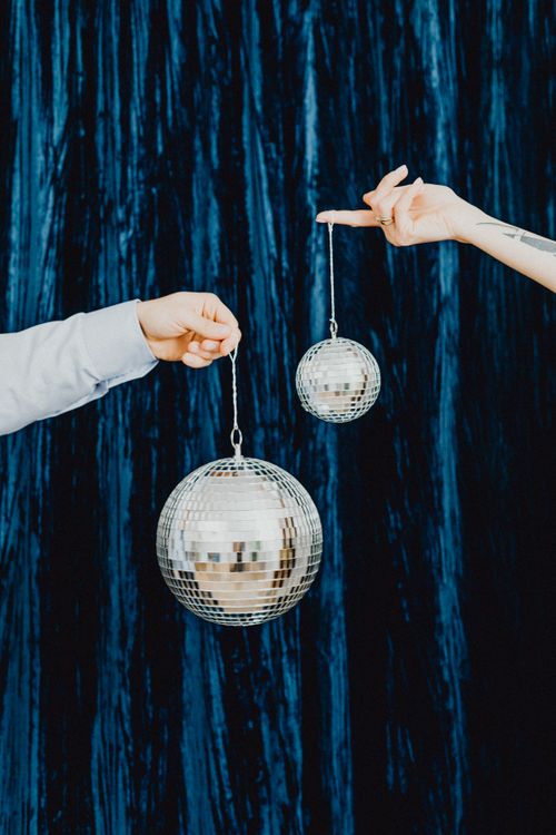Free Two hands hold shiny disco balls against a dark blue curtain background. Stock Photo
