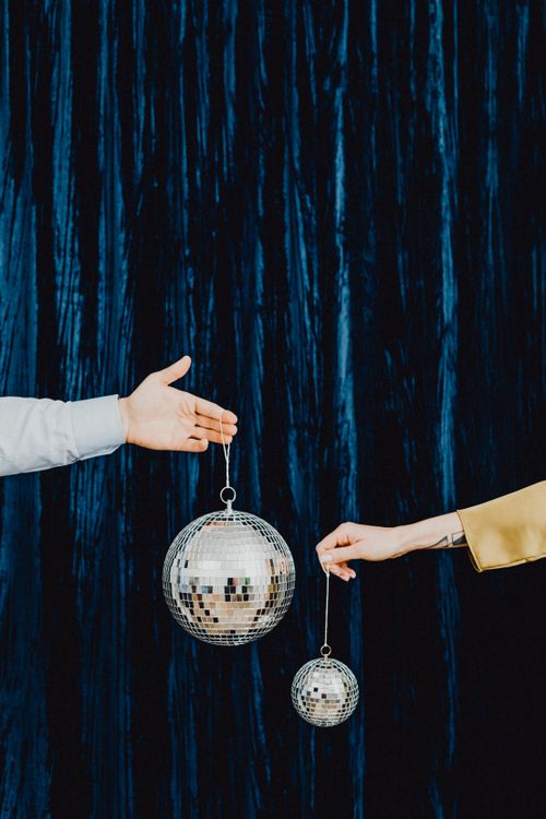 Free A close-up of hands holding shiny silver disco balls against a dark textured curtain backdrop indoors. Stock Photo