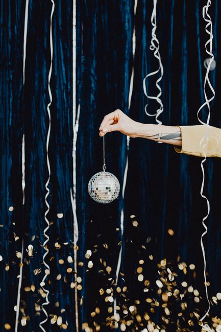 A close-up of a hand holding a disco ball among festive streamers and confetti.