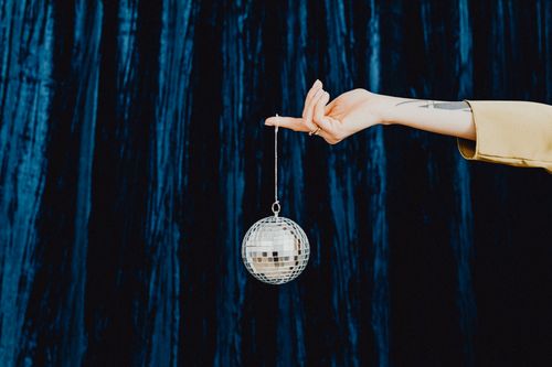 Free A stylish hand holds a sparkling disco ball against a dark blue curtain backdrop. Stock Photo