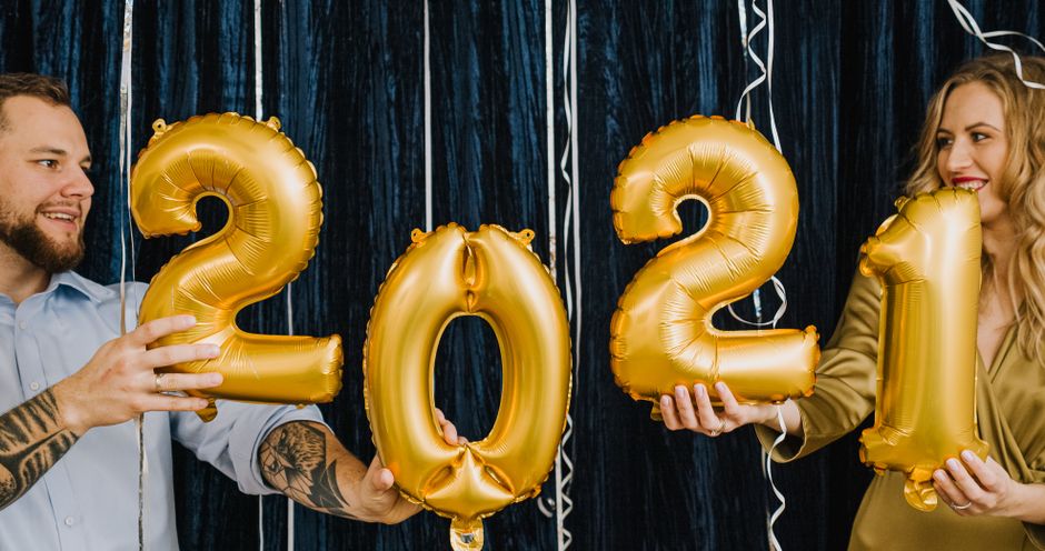 Couple holding gold balloons to celebrate New Year 2021 with smiles indoors.