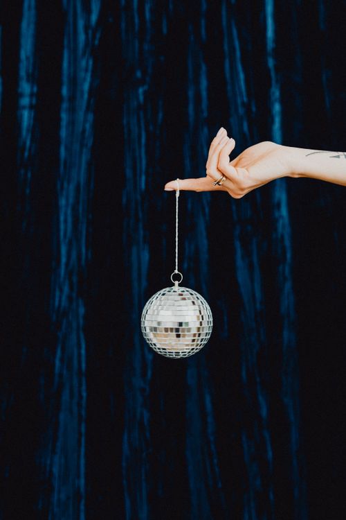 Free A hand delicately holding a shiny silver disco ball against a dark background. Stock Photo