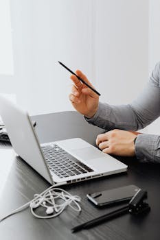 Close-up of a person using a laptop in a modern office setting with electronic devices on the table.