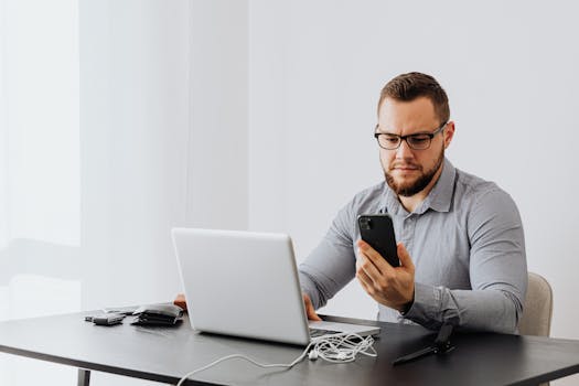 Professional man working at desk with laptop and smartphone, indoors.