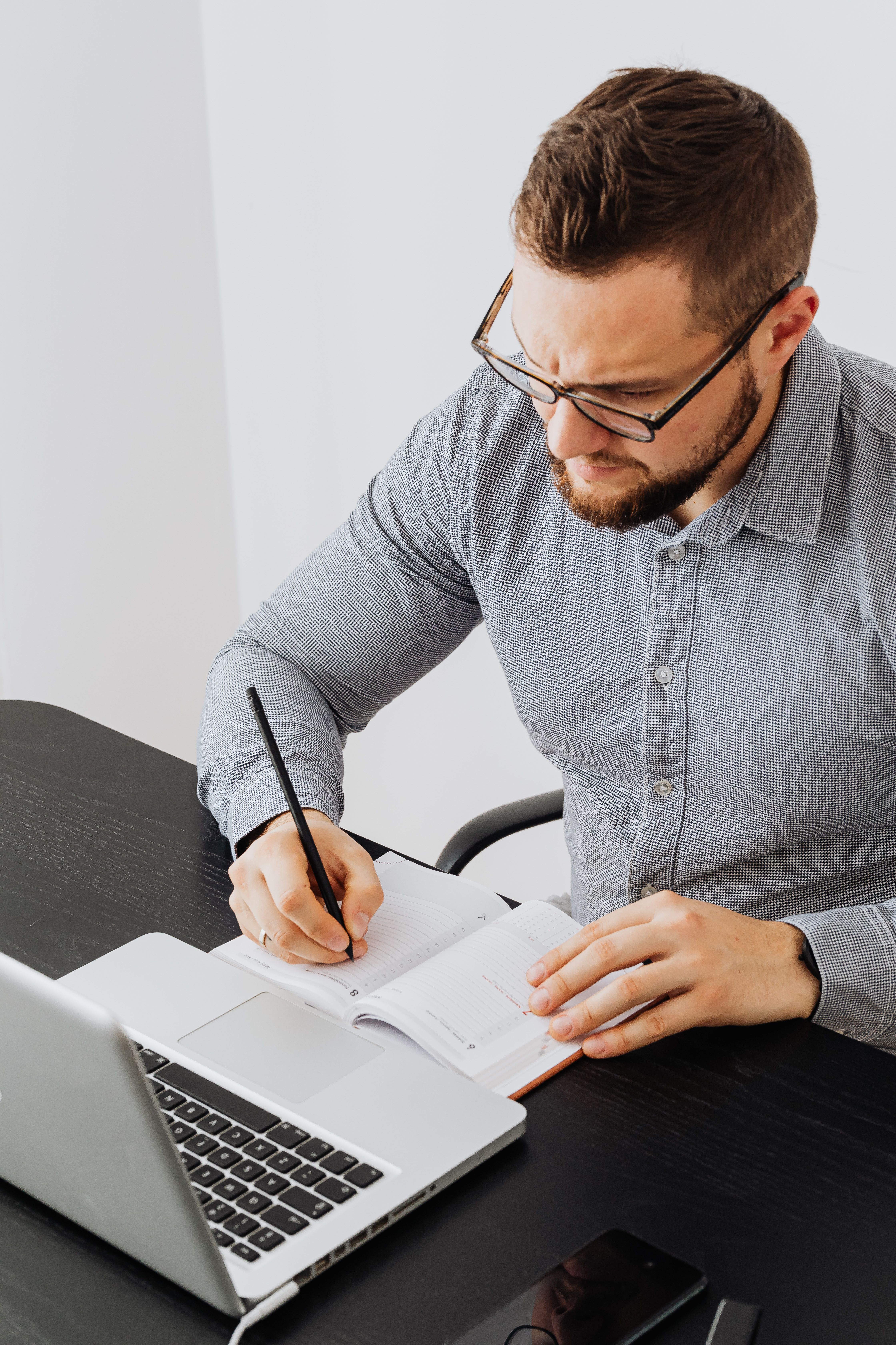 A man writing in a notebook while using a laptop, featuring an office setting for productivity and business.