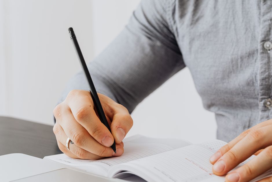 A detailed view of a person writing in a notebook with a pen, showing focus and concentration. A detailed view of a person writing in a notebook with a pen, showing focus and concentration.
