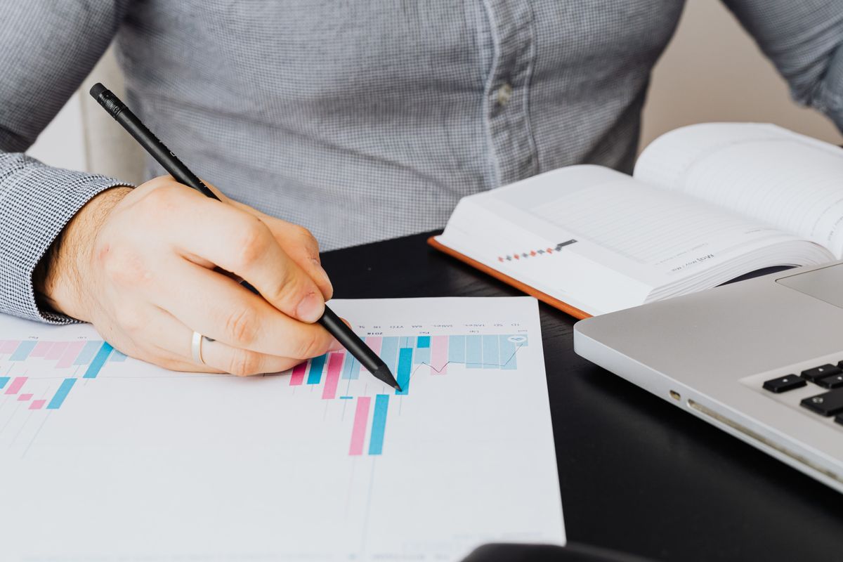 A person reviewing a printed performance chart beside a laptop and an open notebook, scoring content during an audit