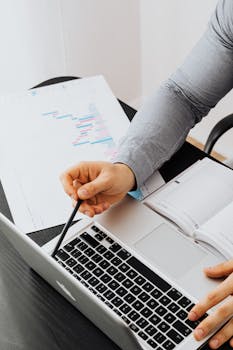 Business professional analyzing charts and data on a laptop in office setting.