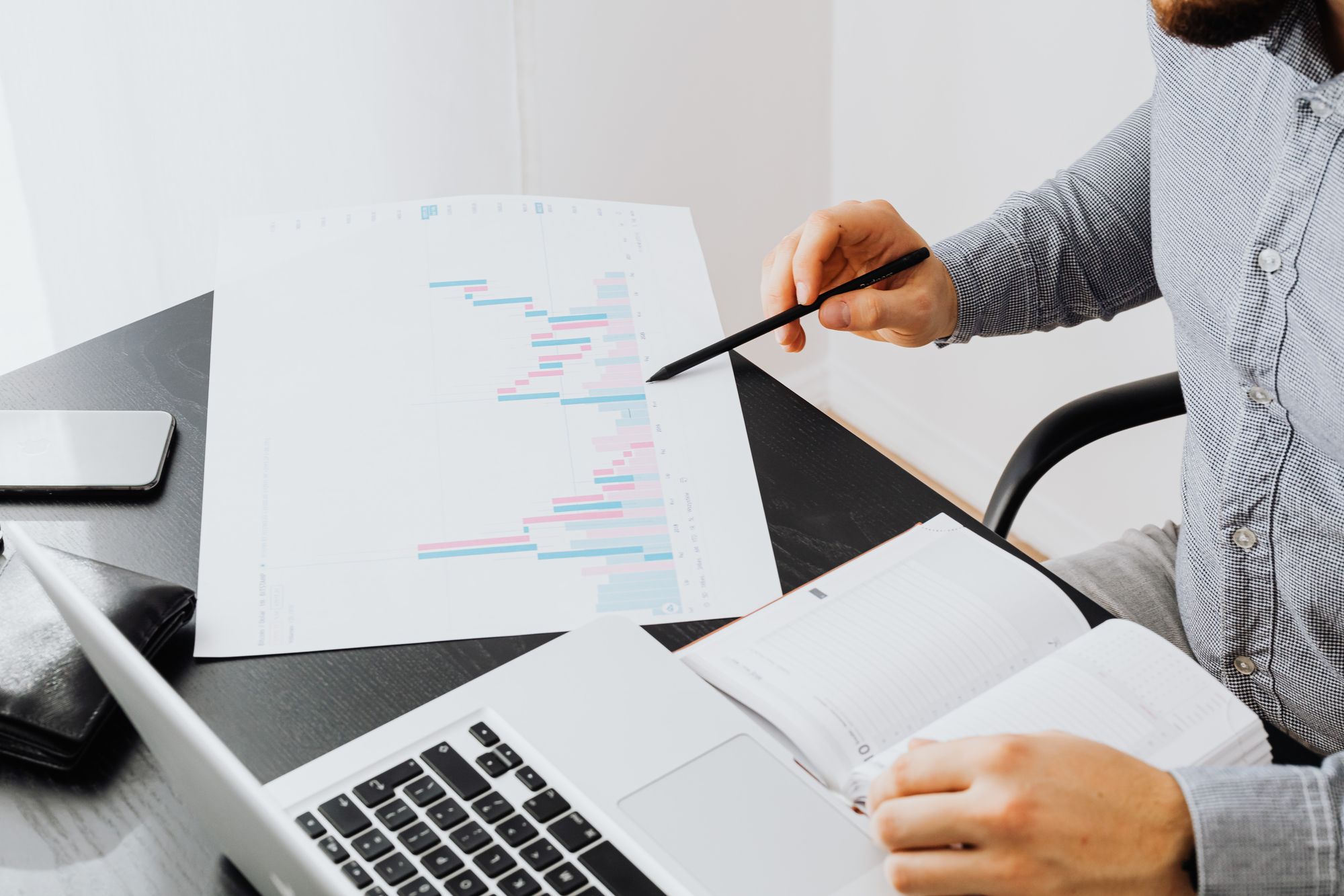 An office setup with a person analyzing a graph printout while using a laptop and notebook.
